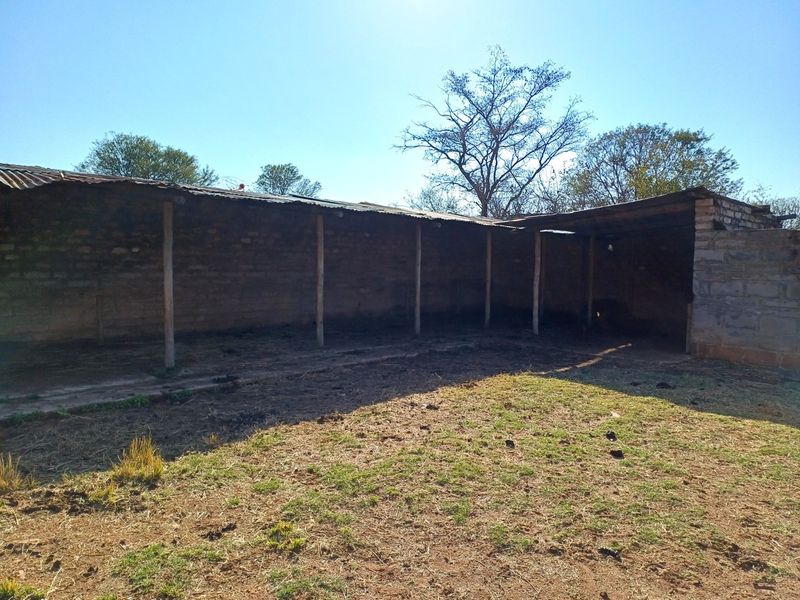 An open-sided farm utility structure featuring brick masonry walls and a corrugated metal roof supported by timber posts.