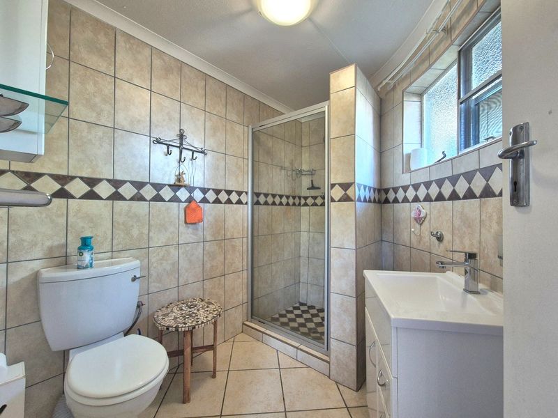 A functional bathroom featuring a shower enclosure, vanity basin, toilet, and neutral tiled finishes throughout.