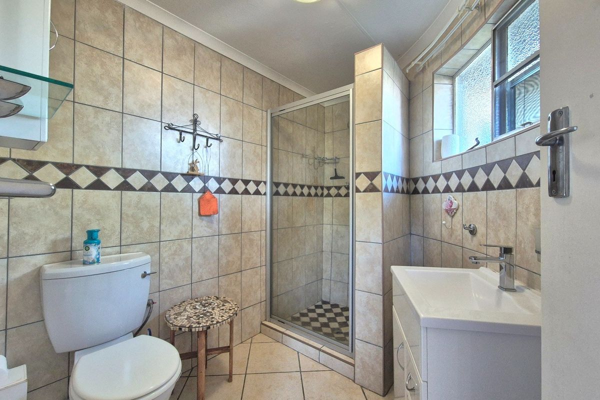 A functional bathroom featuring a shower enclosure, vanity basin, toilet, and neutral tiled finishes throughout.