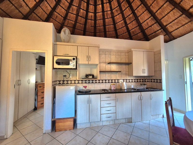 Compact kitchen featuring light wood cabinetry, granite countertops, tiled backsplash, and a distinctive high-pitched thatch roof ceiling.