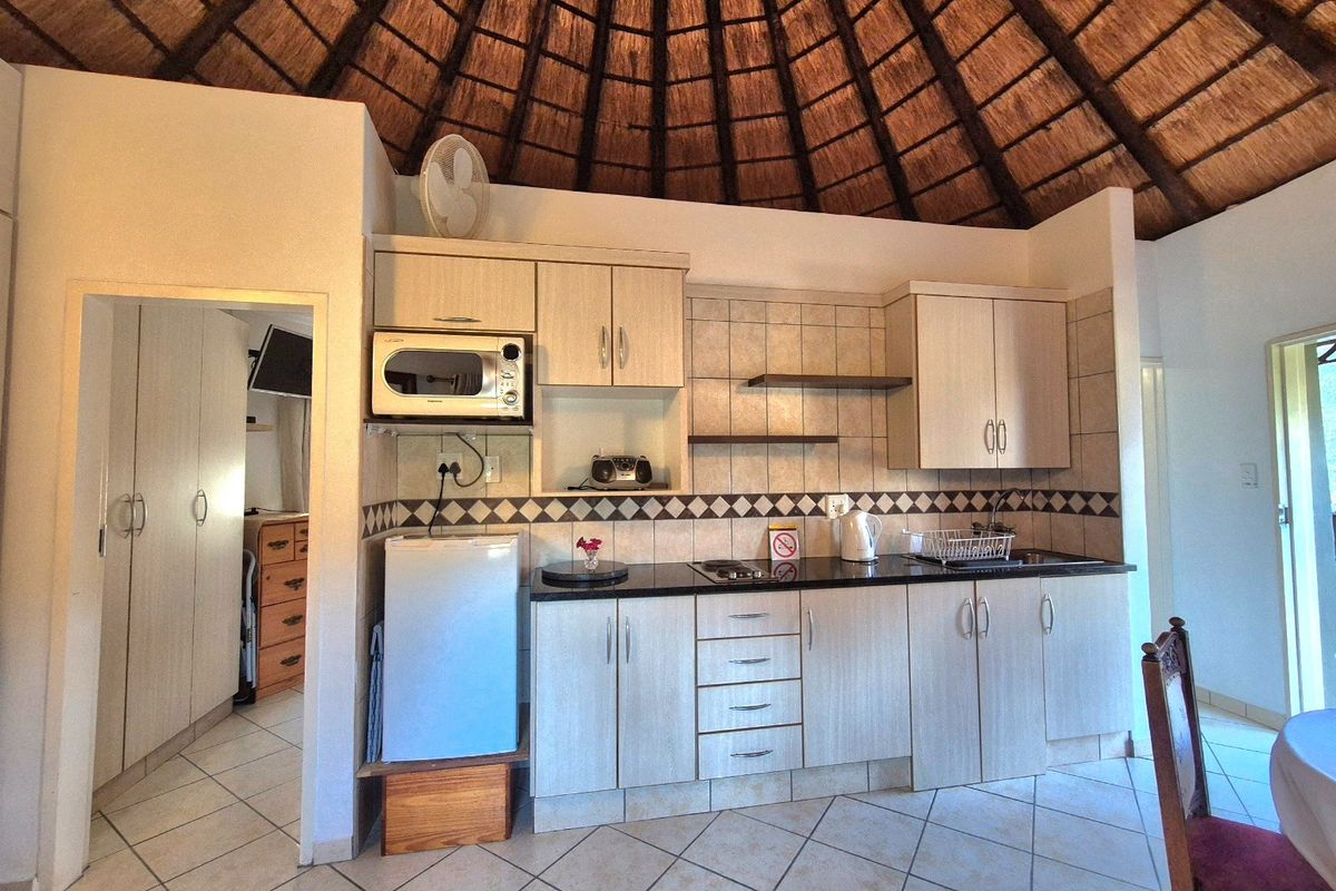 Compact kitchen featuring light wood cabinetry, granite countertops, tiled backsplash, and a distinctive high-pitched thatch roof ceiling.