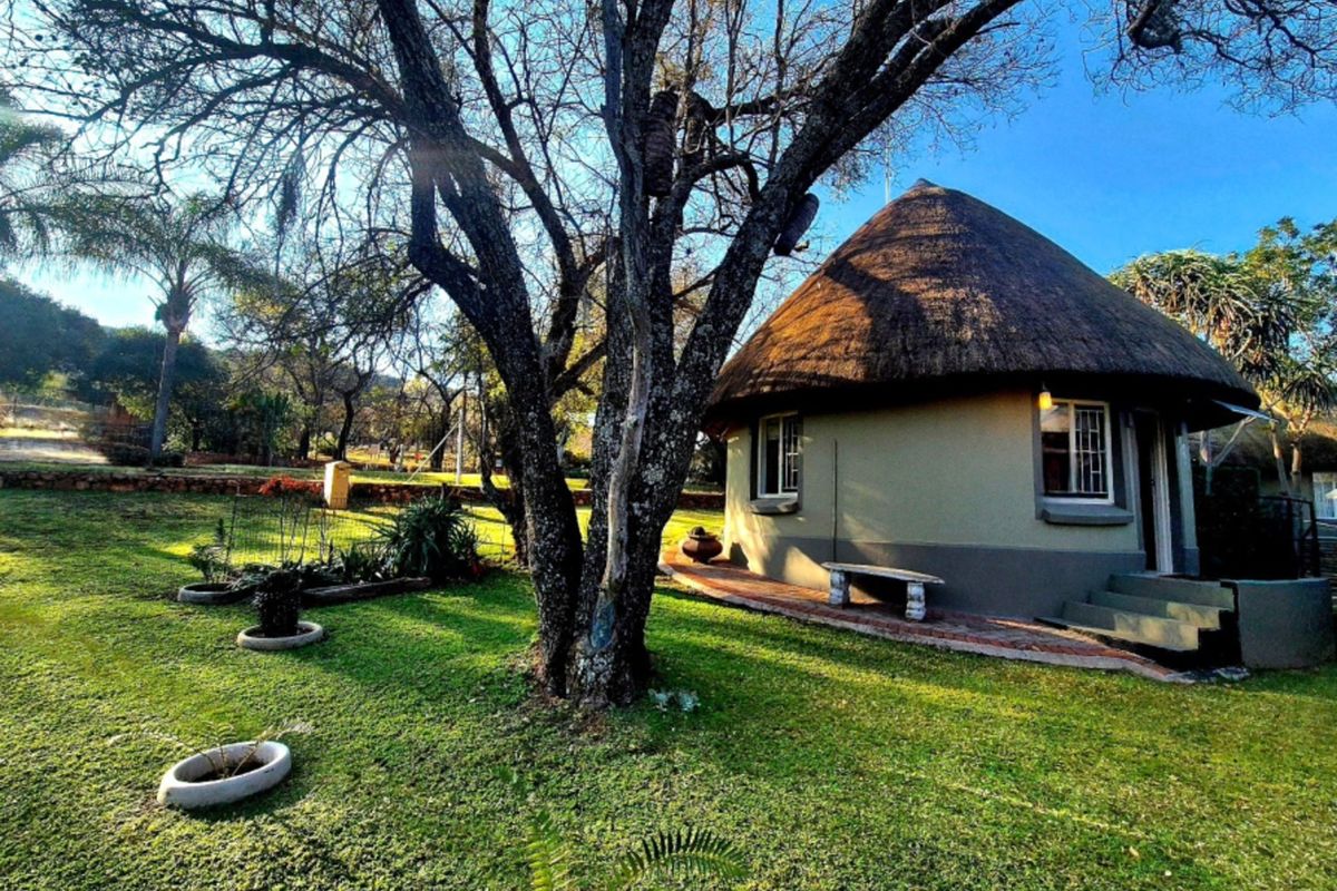 A charming round cottage with a traditional thatch roof, set within a spacious, well-maintained garden with mature trees.
