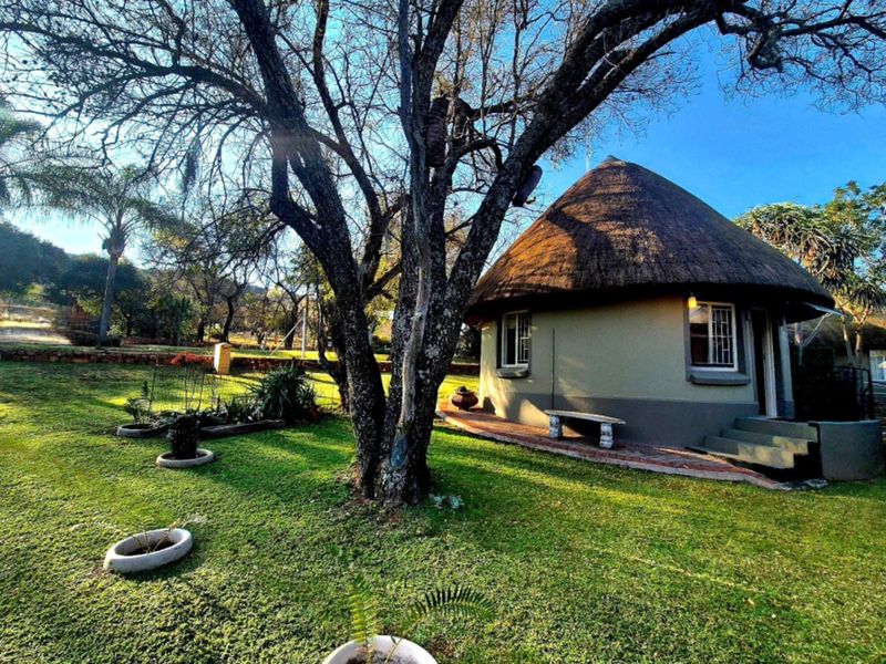 A charming round cottage with a traditional thatch roof, set within a spacious, well-maintained garden with mature trees.