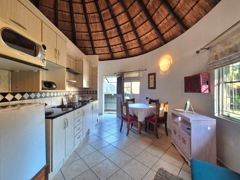 Open-plan kitchen and dining area featuring a unique vaulted thatched ceiling, tiled flooring, and fitted cabinetry with granite countertops.
