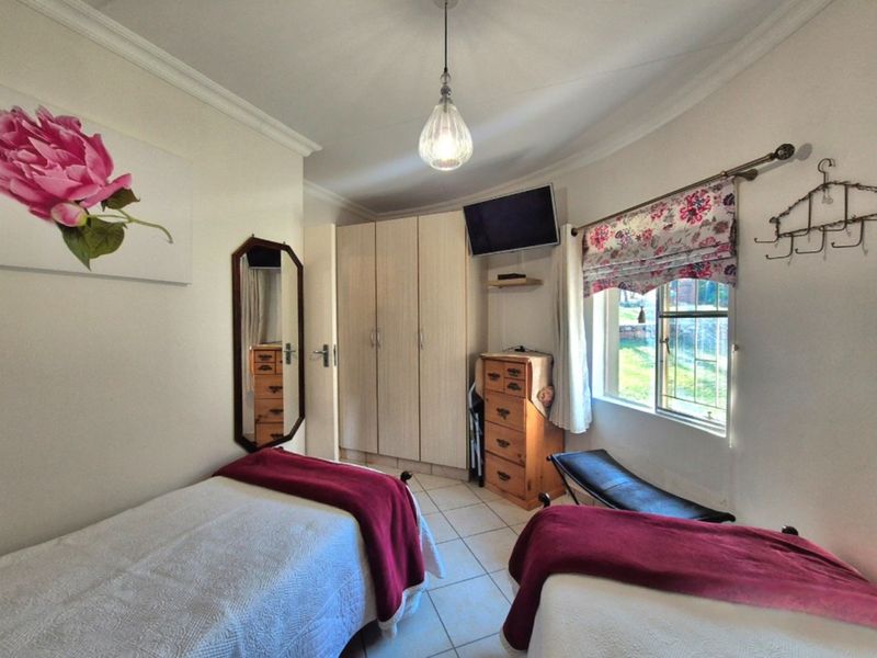 A functional bedroom featuring built-in cupboards, tiled flooring, and natural light through a window with security bars.