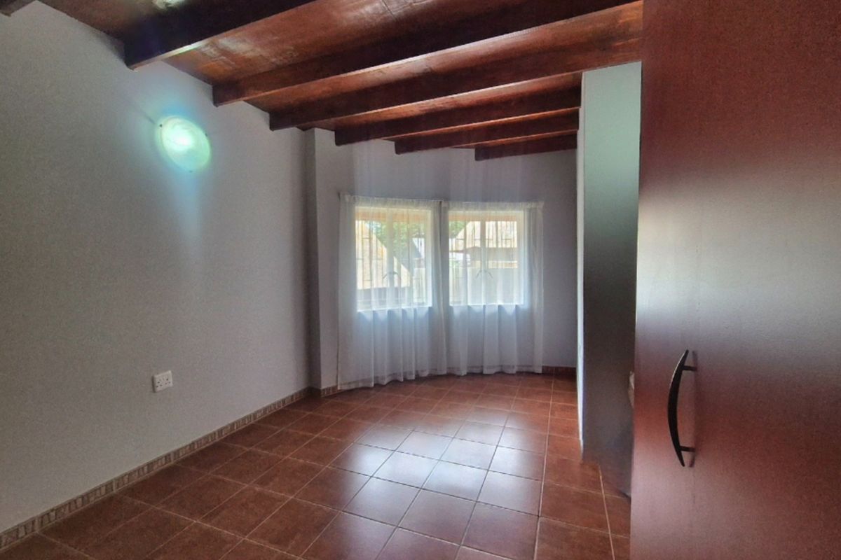 An empty bedroom featuring exposed timber ceiling beams, tiled flooring, and a built-in cupboard, offering a clean and neutral space.