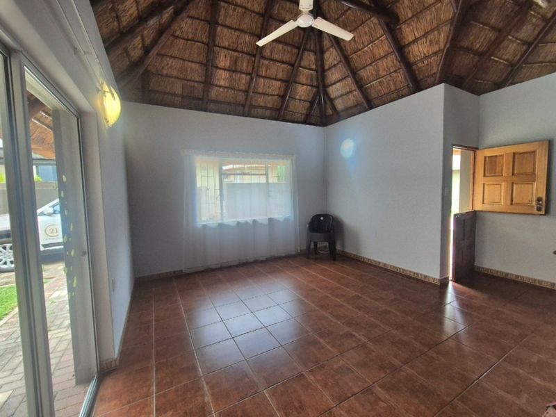 Spacious living area featuring a high vaulted thatched ceiling, tiled flooring, and direct access to the exterior through a sliding glass door.