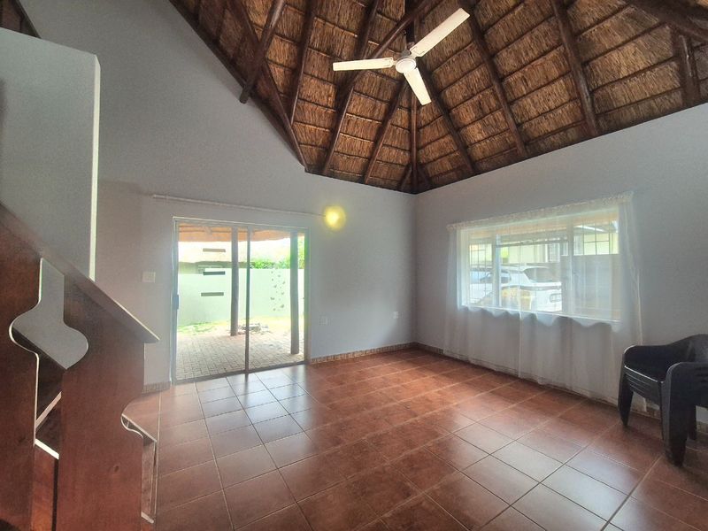 Spacious living area featuring a high vaulted thatched ceiling with exposed rafters, tiled flooring, and direct access to an outdoor patio through sliding doors.