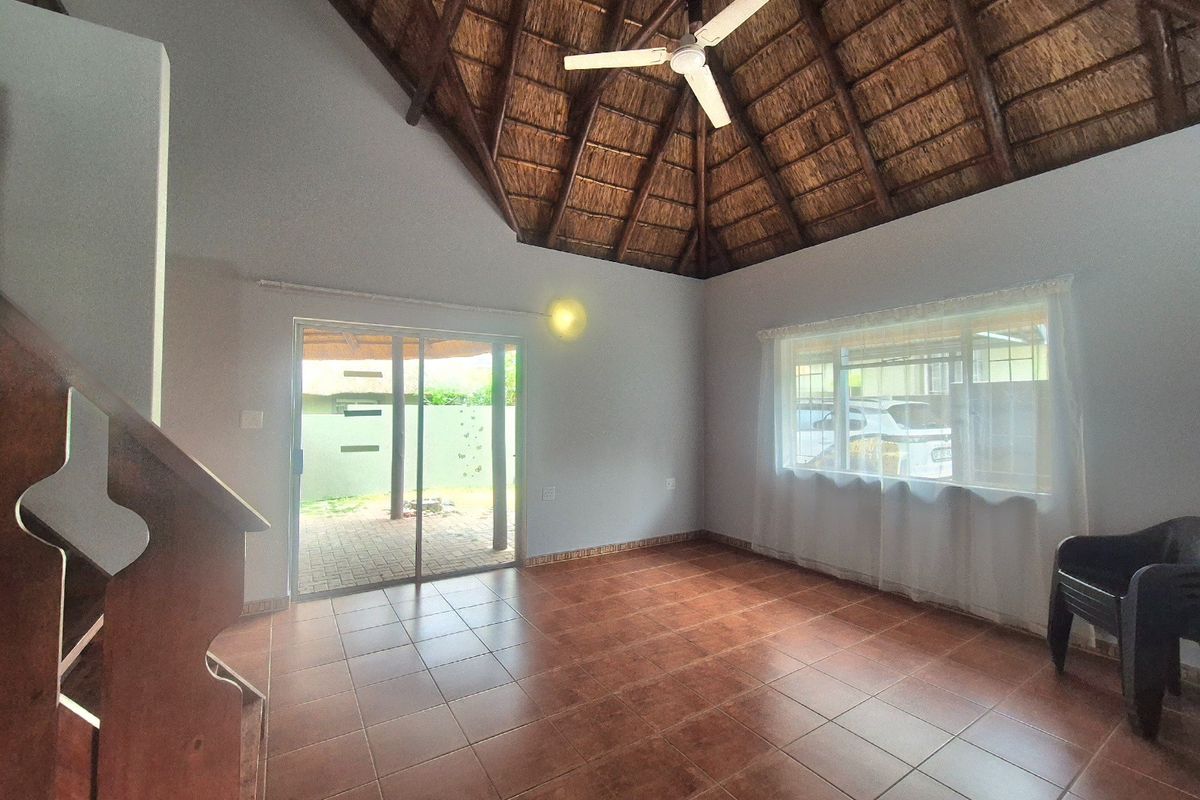 Spacious living area featuring a high vaulted thatched ceiling with exposed rafters, tiled flooring, and direct access to an outdoor patio through sliding doors.