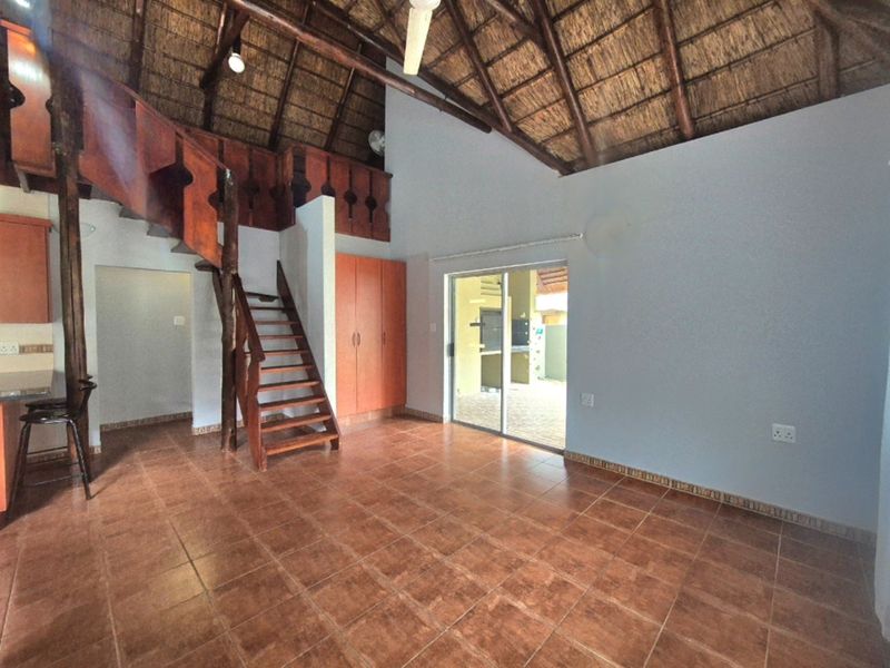 Open-plan living area featuring a high thatched ceiling with exposed rafters, tiled flooring, a wooden staircase, and direct access to an outdoor patio.