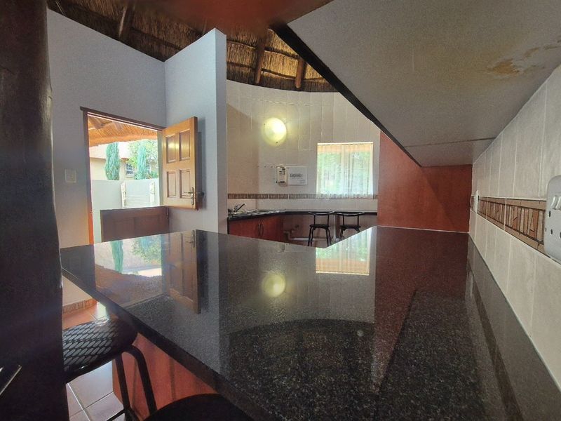 Kitchen area featuring a granite breakfast bar, tiled backsplash, and a unique thatched roof ceiling, with direct access to an outdoor patio area.