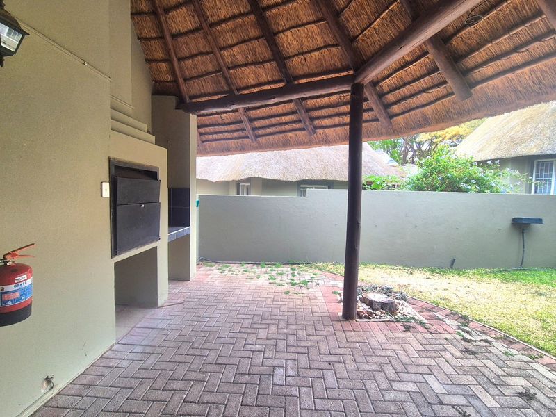 Covered outdoor patio featuring a built-in braai, traditional thatch roof, and paved flooring, offering a functional space for outdoor entertaining.