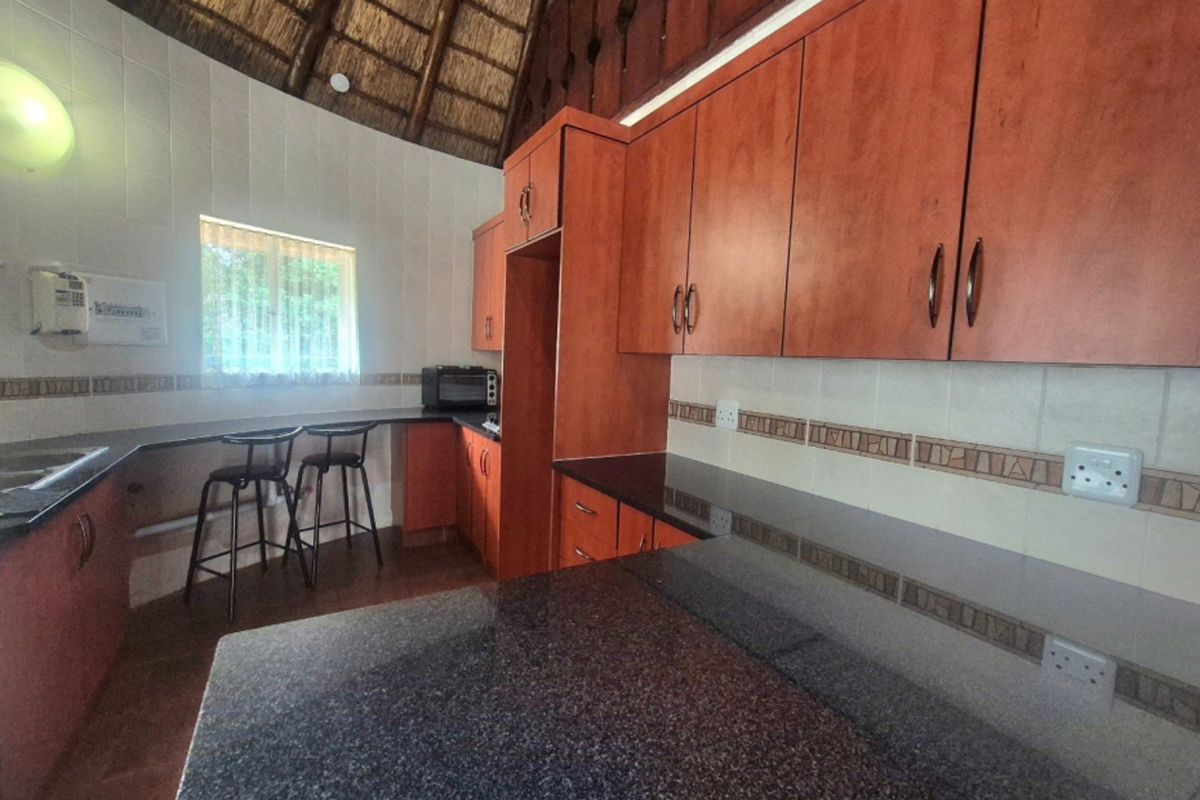 Kitchen featuring granite countertops, ample wooden cabinetry, tiled backsplash, and a unique high-pitched thatch roof ceiling.