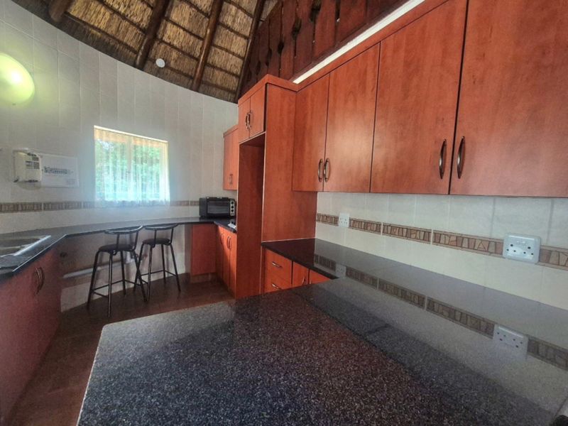Kitchen featuring granite countertops, ample wooden cabinetry, tiled backsplash, and a unique high-pitched thatch roof ceiling.
