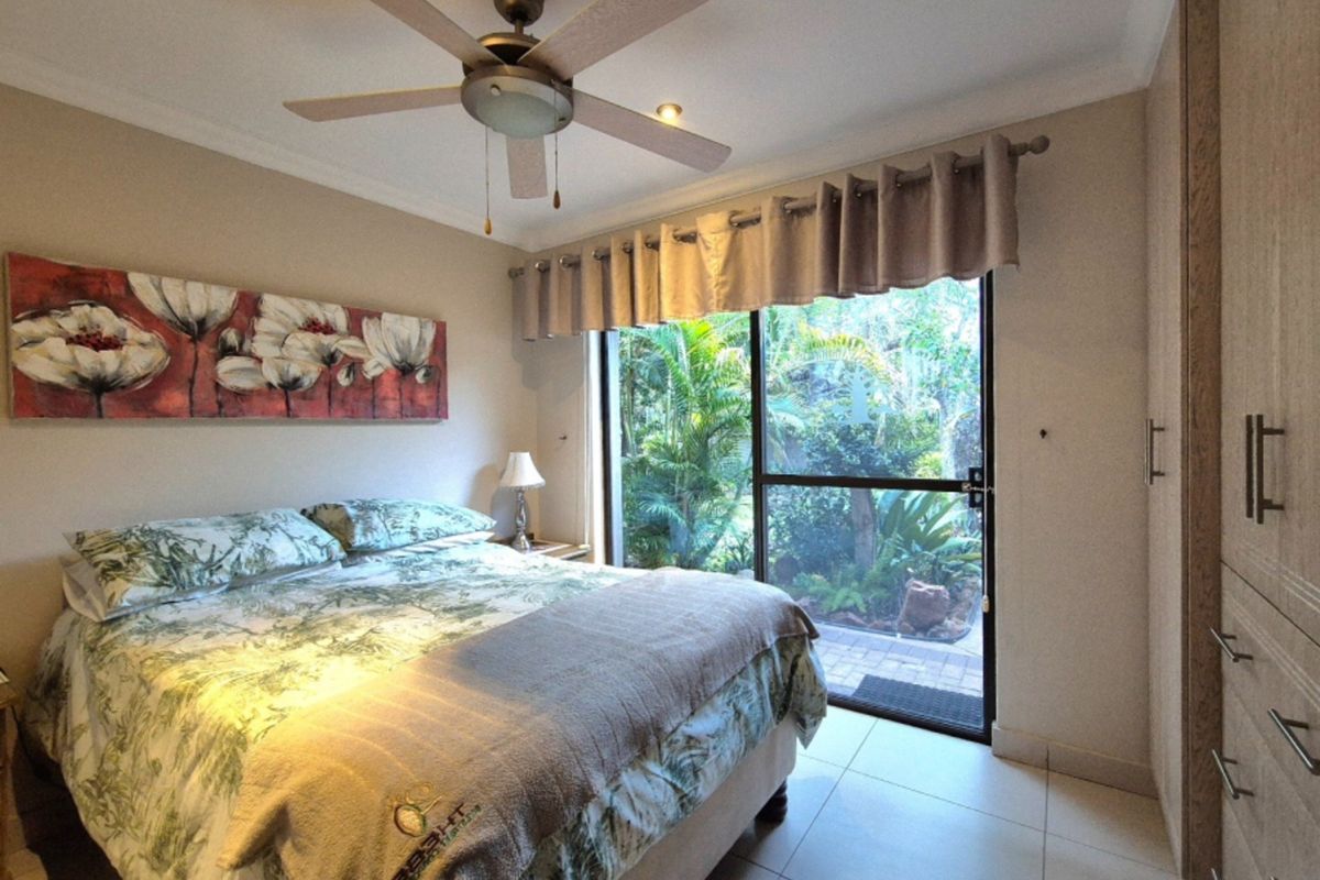 A well-maintained bedroom featuring tiled flooring, built-in cupboards, a ceiling fan, and direct access to a private garden through a sliding glass door.