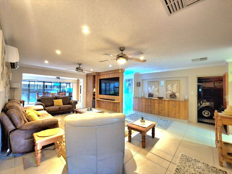Spacious living room featuring tiled flooring, built-in wooden cabinetry, ceiling fans, and integrated air conditioning, offering a comfortable and functional layout.