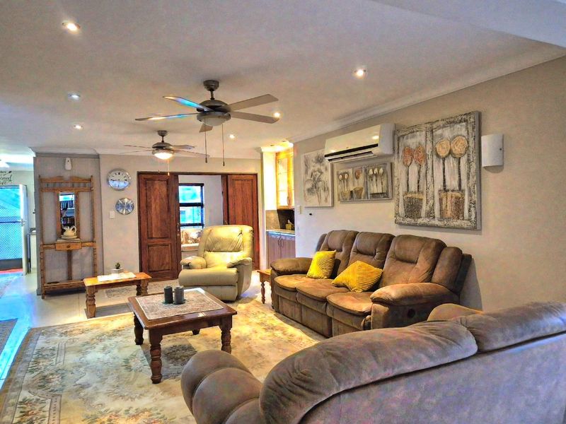 Spacious living room featuring tiled flooring, recessed downlights, ceiling fans, and a wall-mounted split-system air conditioning unit.