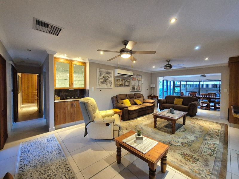 Spacious open-plan living area featuring a built-in bar, tiled flooring, ceiling fans, and direct access to an adjoining dining space.