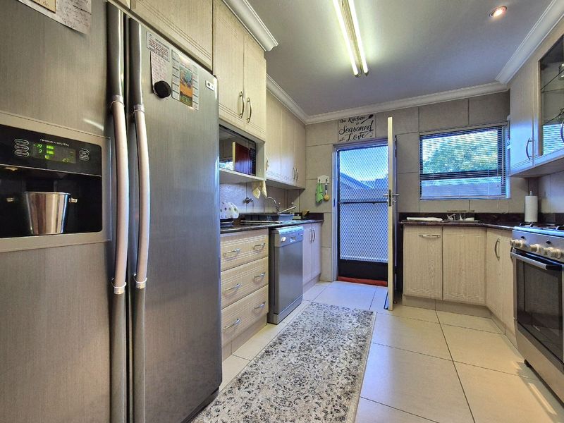 A functional kitchen featuring light wood-finish cabinetry, granite countertops, stainless steel appliances, and direct access to the exterior via a security door.