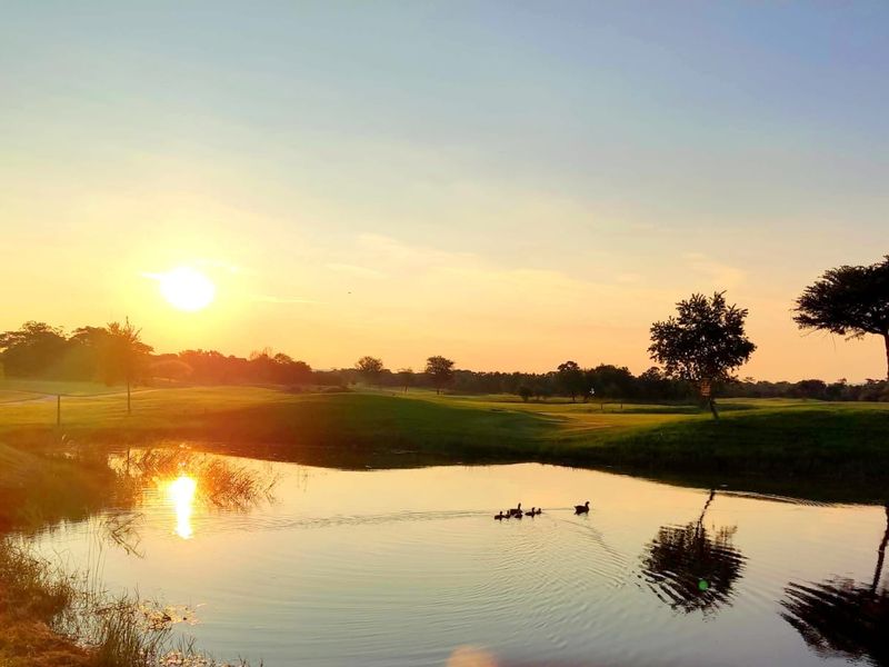 A scenic view of a tranquil pond set within expansive, well-maintained residential grounds at sunset.
