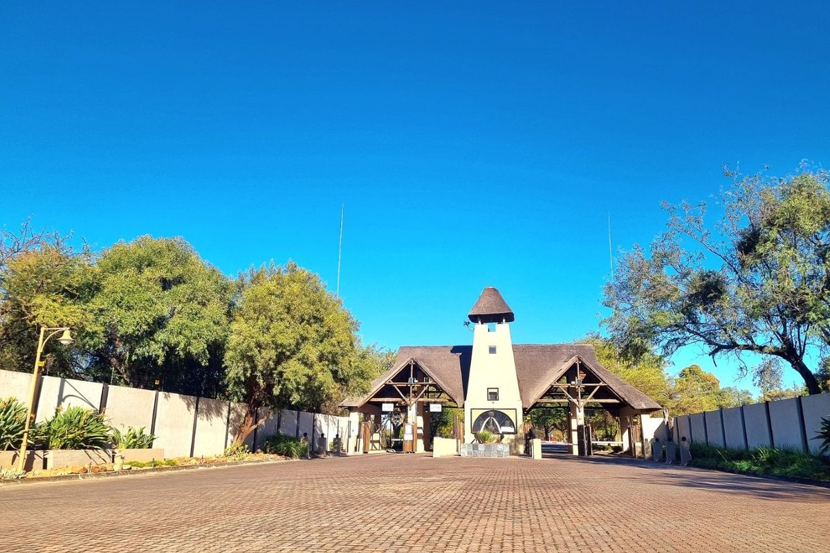 A well-maintained residential estate entrance featuring a prominent security gatehouse with a thatched roof and extensive paved driveway access.