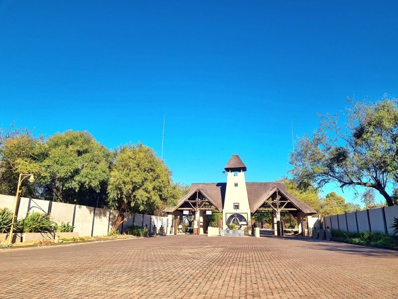 A well-maintained residential estate entrance featuring a prominent security gatehouse with a thatched roof and extensive paved driveway access.