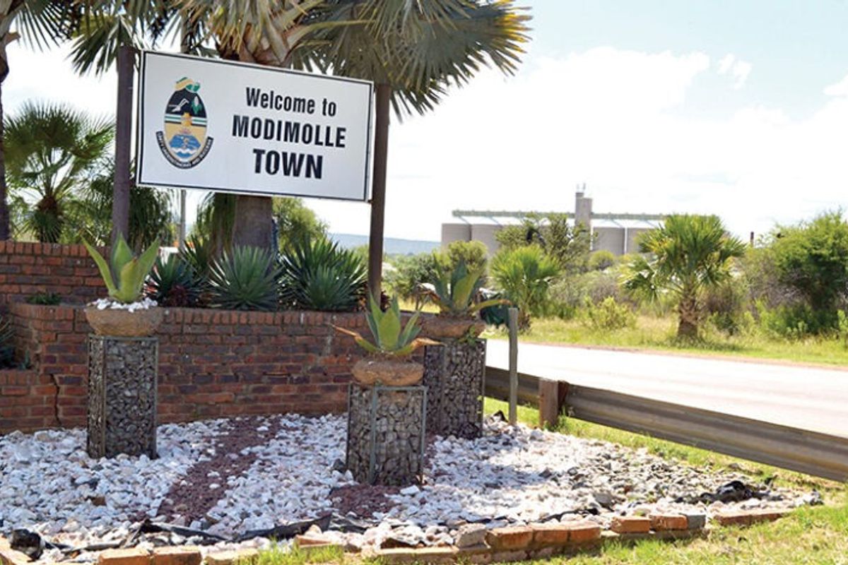 A roadside welcome sign for Modimolle Town featuring brick retaining walls and decorative gabion planters.