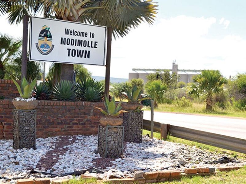 A roadside welcome sign for Modimolle Town featuring brick retaining walls and decorative gabion planters.