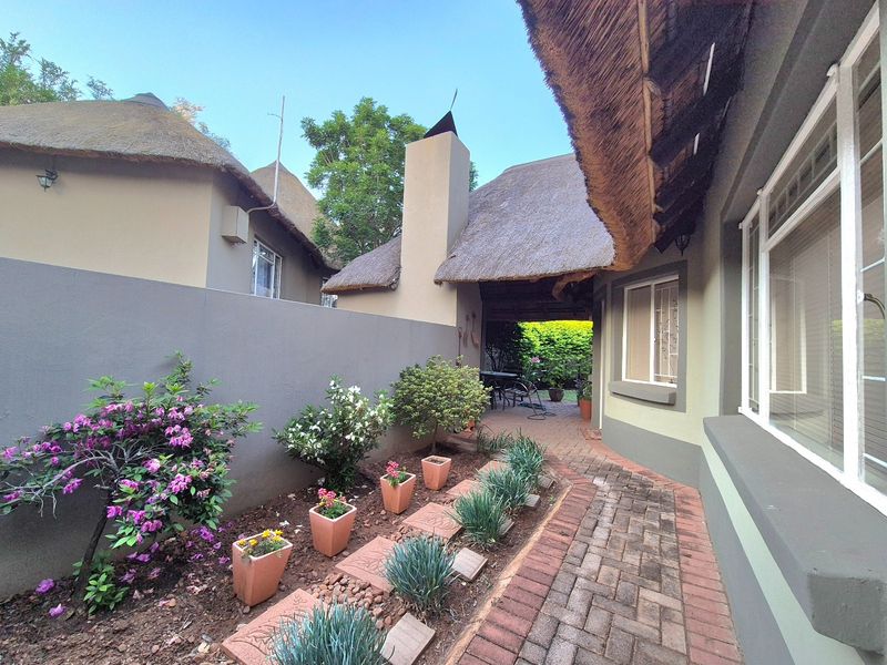 A well-maintained rear exterior area featuring a traditional thatch roof, brick paved pathway, and a private garden space with a masonry chimney.