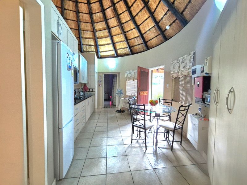 Open-plan kitchen and dining area featuring a unique vaulted thatched ceiling, tiled flooring, and built-in cabinetry with direct access to the outdoors.
