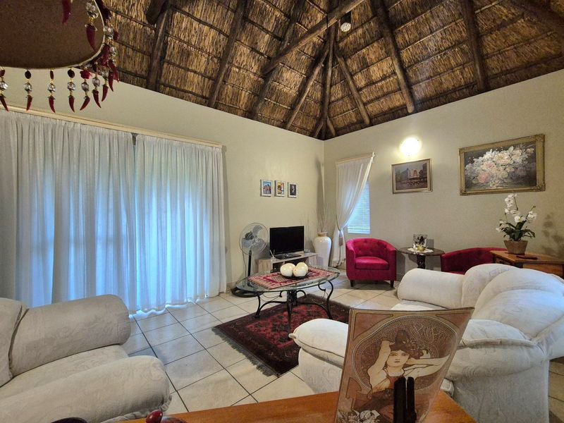 A living room featuring a high vaulted thatched roof with exposed timber rafters, tiled flooring, and large sliding glass doors leading to the exterior.