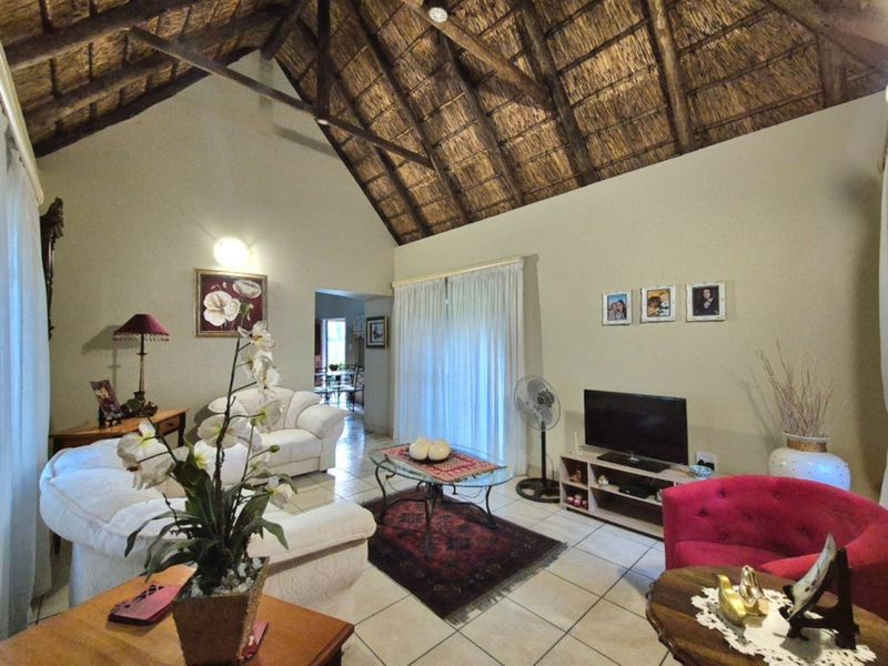 Spacious living room featuring a high vaulted exposed thatch ceiling with timber trusses and tiled flooring, leading out through sliding glass doors.