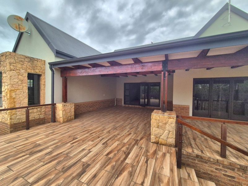 A spacious covered patio featuring wood-look tile flooring, a timber pergola, and stone-clad pillars, offering a seamless transition to the home's interior.