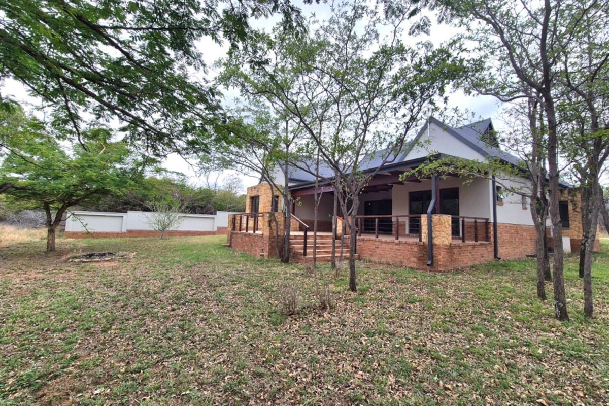 Rear view of a house featuring a brick and stone facade, a covered patio with timber decking, and a surrounding garden area.