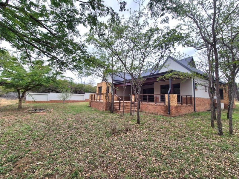 Rear view of a house featuring a brick and stone facade, a covered patio with timber decking, and a surrounding garden area.