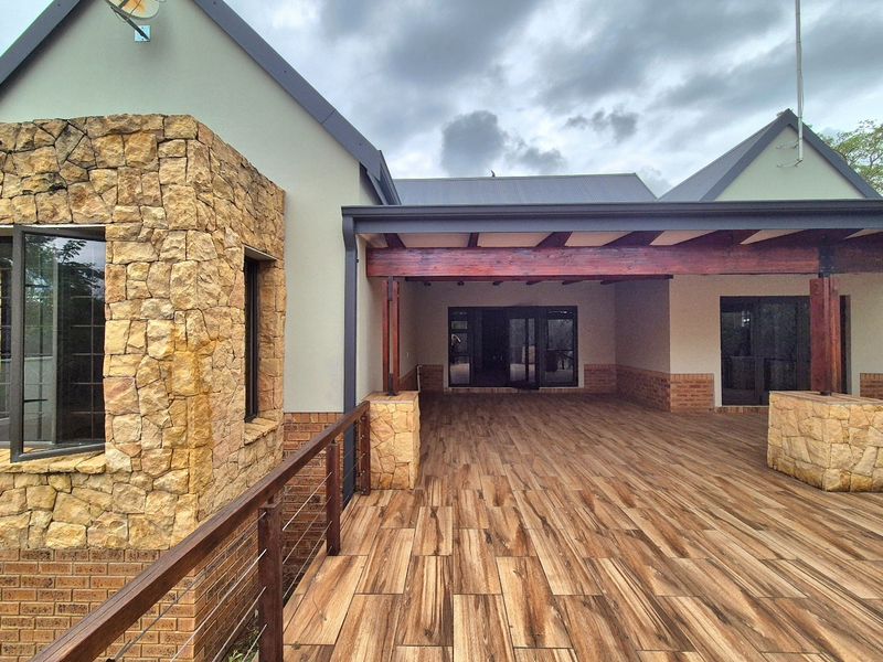 Spacious covered patio featuring wood-look tiled flooring, stone cladding accents, and a timber pergola, providing a seamless transition to the interior living space.