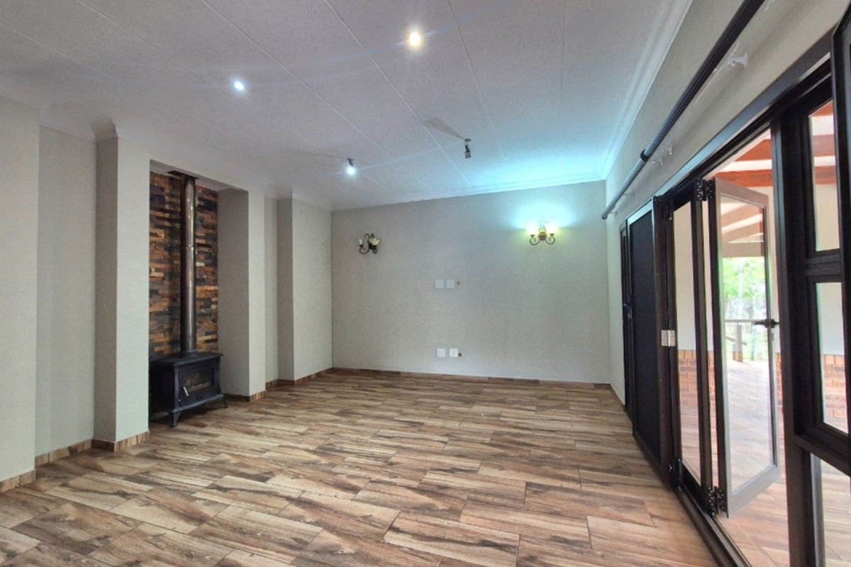 Spacious living room featuring wood-look tile flooring, a stone-clad wood-burning fireplace, and large bi-fold doors opening to the outdoor area.