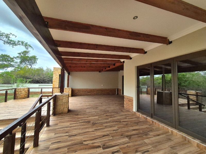 Spacious covered patio featuring exposed timber beams, tiled flooring, and stone-clad pillars, offering a seamless transition to the outdoor garden area.