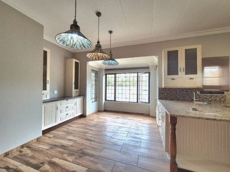 Spacious kitchen featuring granite countertops, ample built-in cabinetry, mosaic tile backsplash, and wood-look tiled flooring with large windows providing natural light.
