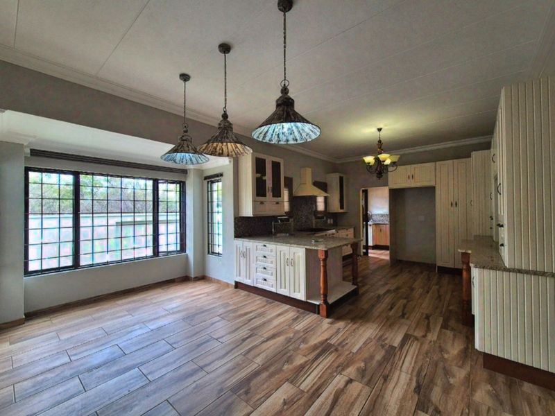 Spacious kitchen featuring granite countertops, ample built-in cabinetry, wood-look tiled flooring, and large windows with security bars.