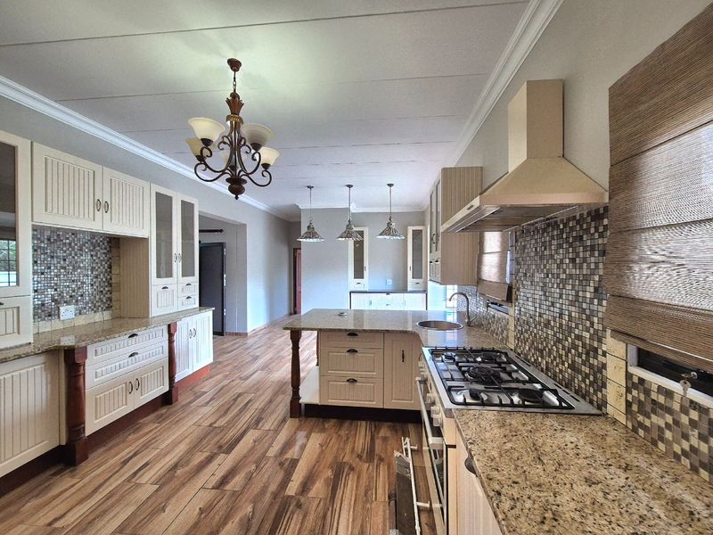 Spacious kitchen featuring granite countertops, a central island, gas hob with extractor, and mosaic tile backsplash, finished with warm-toned laminate flooring.