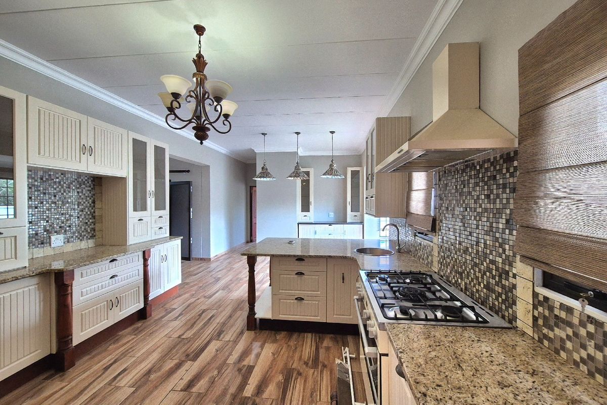 Spacious kitchen featuring granite countertops, a central island, gas hob with extractor, and mosaic tile backsplash, finished with warm-toned laminate flooring.