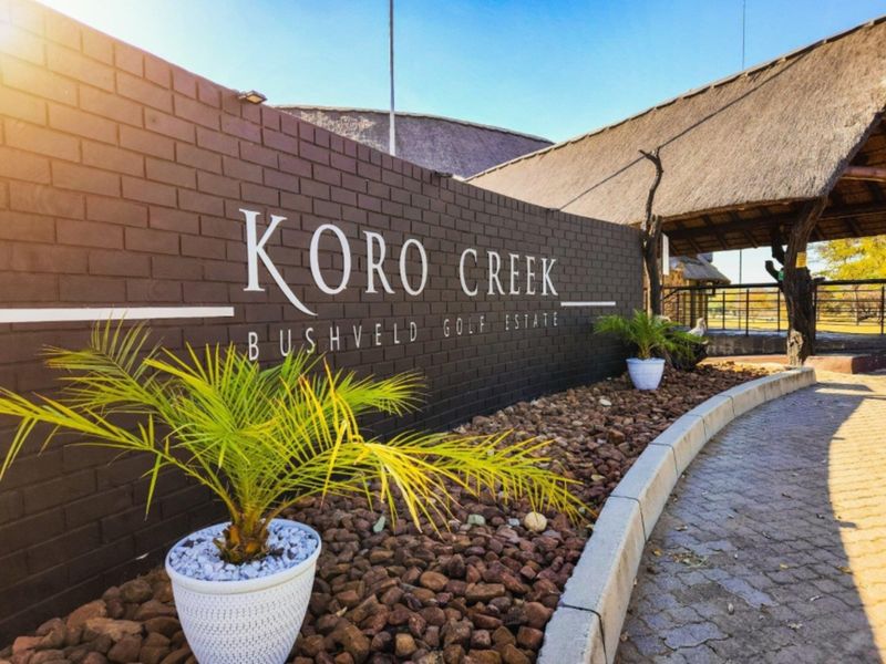 Entrance signage and landscaped boundary wall at Koro Creek Bushveld Golf Estate, featuring paved walkways and traditional thatched roof architecture.