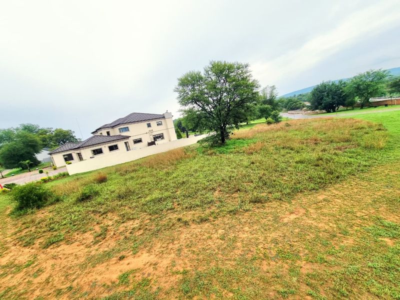 A view of a residential plot featuring open grass land with a neighboring house and boundary wall visible in the background.