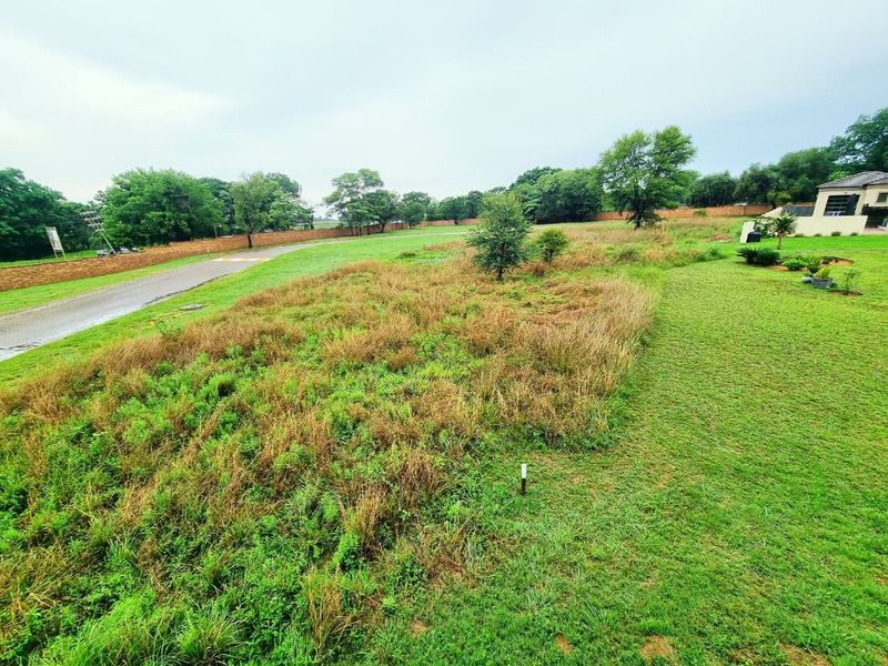A view of a vacant residential plot featuring a paved road, boundary wall, and established lawn area.
