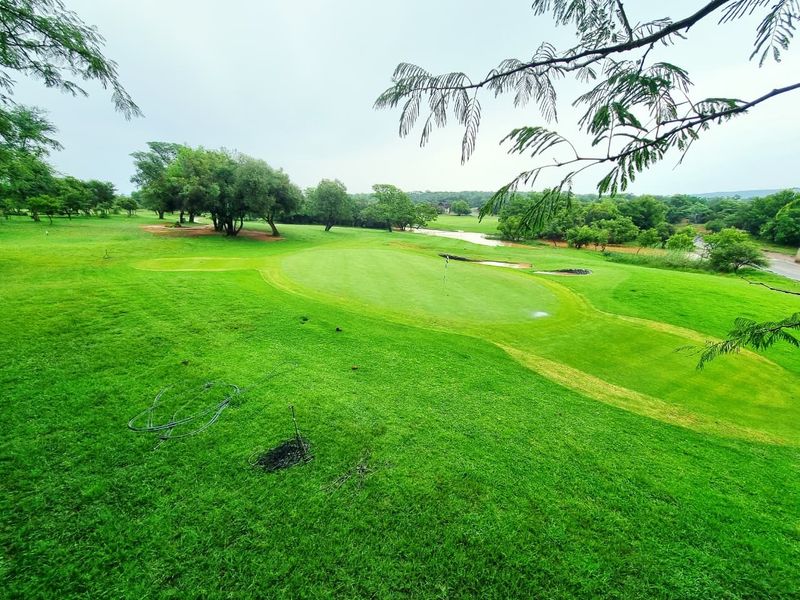A scenic view overlooking a well-maintained golf course with lush green fairways, putting greens, and mature trees.