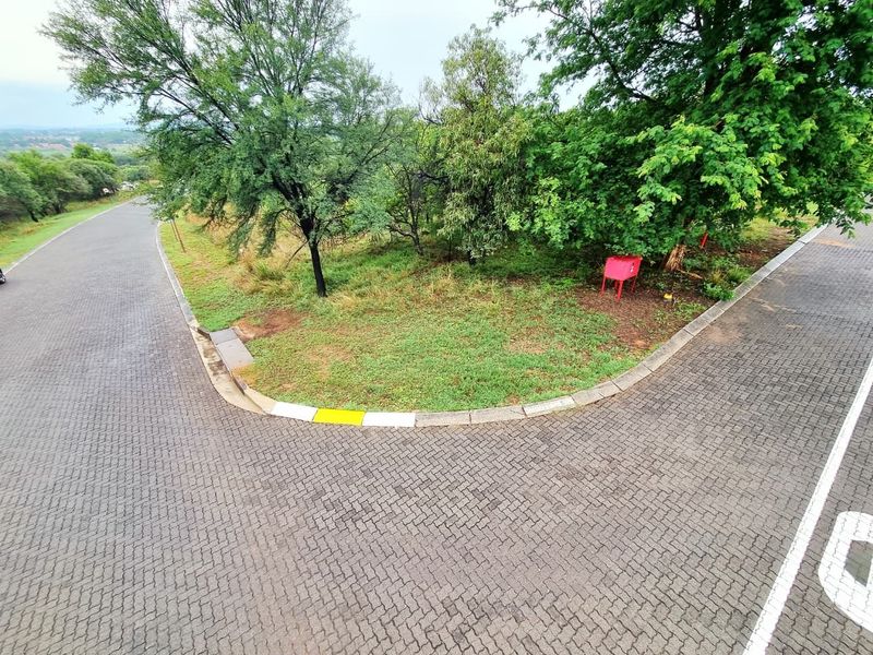 An elevated view of a residential street corner featuring paved roads, concrete curbing, and established trees on a vacant plot.