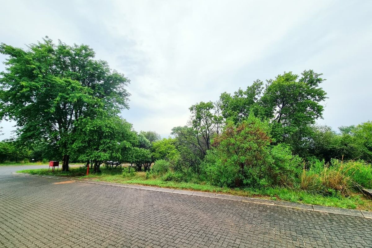 A view of a residential vacant land plot featuring a paved driveway and established mature trees, offering a natural setting for potential development.
