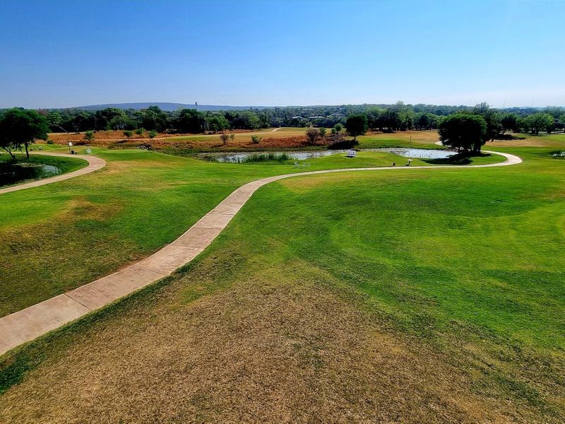 A scenic elevated view of a well-maintained golf course featuring lush green fairways, water hazards, and winding paved pathways.