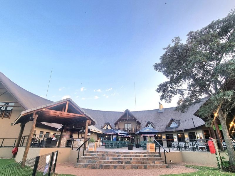 A spacious outdoor patio area featuring a thatched roof structure, stone stairs, and paved flooring, ideal for entertainment and social gatherings.